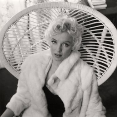 Marilyn Monroe looks pensive sat against a wicker chair in a black and white image