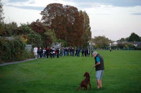 A small gaggle of away fans are escorted through a nearby park into the back entrance of the ground