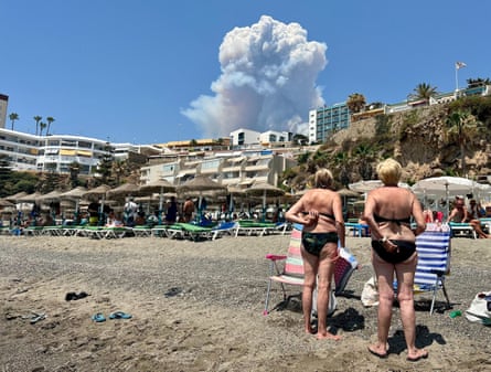 Beachgoers in Torremolinos watch a huge wildfire smoke plume rising in the distance