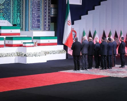 Men in dark suits stand in front of coffins draped in the Iranian flag