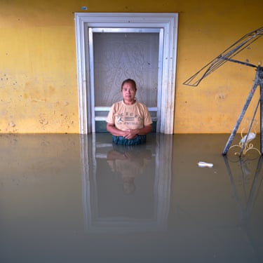A woman stands next to a doorway in a yellow wall waist-deep in flood water