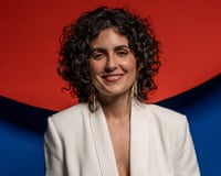 A portrait of Gaia Wilmer in white jacket, against a striking red and blue background