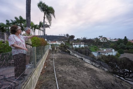 A man and woman stand at the top of a dirt ridge, pointing out over it.