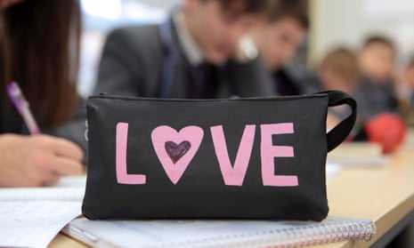 A pencil case with the word 'love' sits on a school pupil's desk.