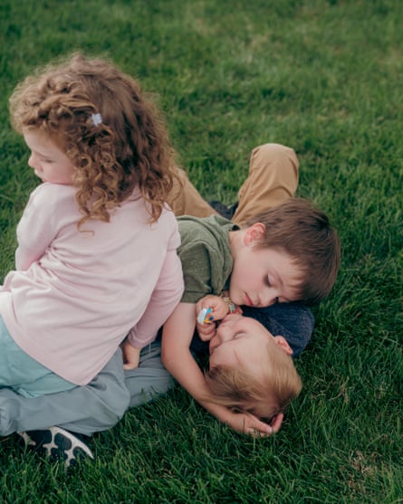 Three children play with each other on a grass lawn