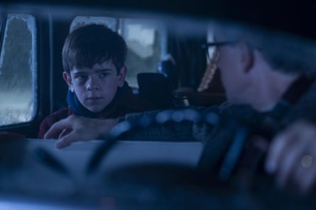 A boy looks nervous in the back seat of a car as the driver turns towards him.