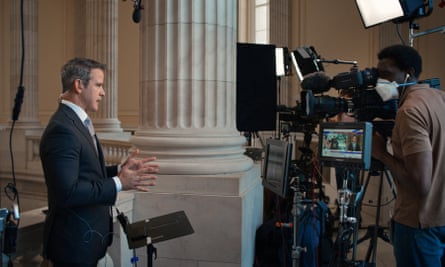 man in a suit speaking to a film camera with a man behind it