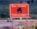 car drives by sign next to road reading 'Bear Country: All bears are dangerous, use extreme caution'