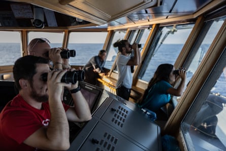 People sit looking out to sea through binoculars.