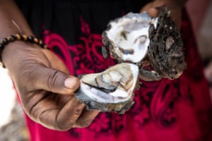 A woman holds open an oyster shell, showing the mollusc