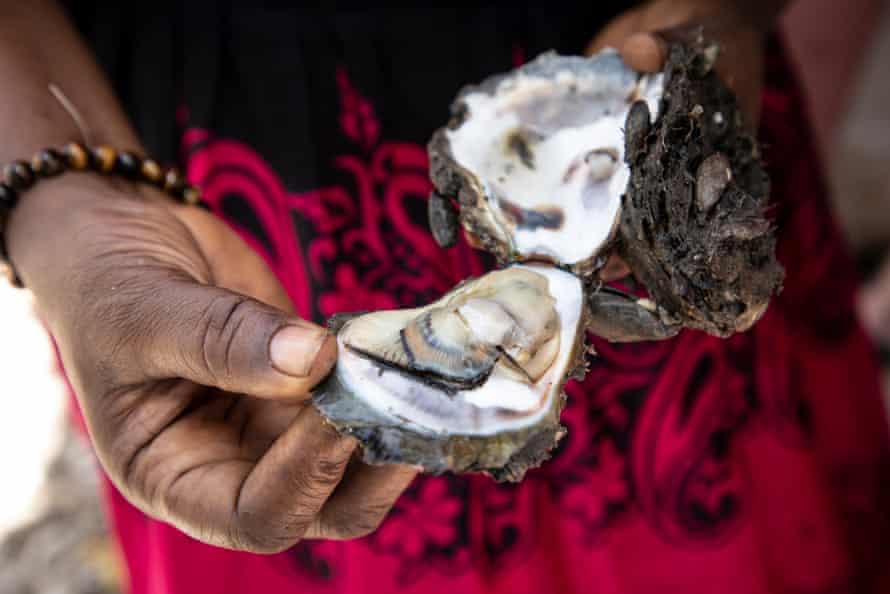 A woman holds open an oyster shell, showing the mollusk