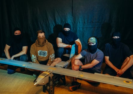 Men wearing masks posing for a portrait next to a Sych mid-strike drone