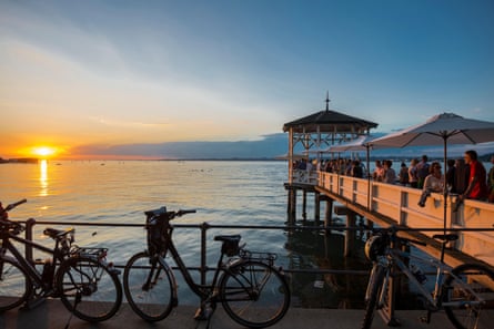 People on a wooden jetty over a lake at sunset, with bikes leaning against a fence