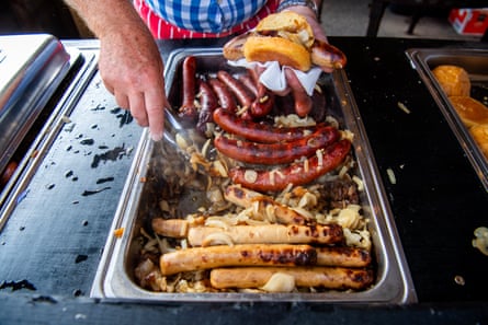 Close-up of a variety of sausages cooking in a tray with onions, and one being placed in a bun