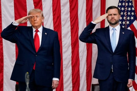 two men in suits stand and salute with large american flag hanging behind them
