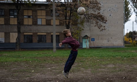 A boy plays football next to a school with boarded-up windows after a Russian missile attack nearby, in Zaporizhzhia oblast, Ukraine.
