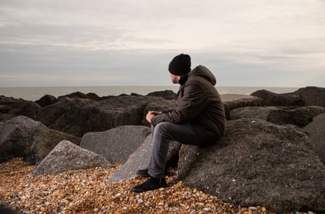 Khaled, a Kuwaiti Bidoon and a former shepherd, sitting on a rock on a pebble beach in Folkestone, Kent
