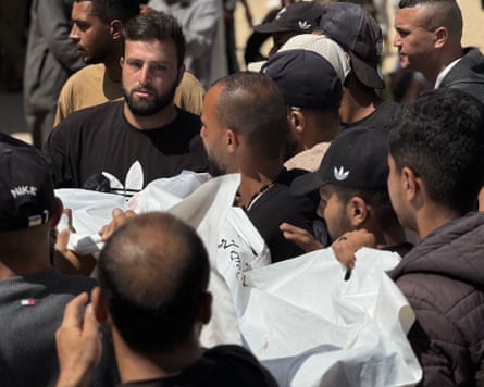 Men in black T-shirts carry a white shroud
