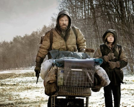 Man with gun and child push shopping trolley along snowy road