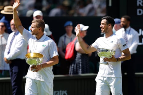 Julian Cash (right) and Lloyd Glasspool (left) wave to the crowd as they hold their Gentlemen's Doubles trophies.