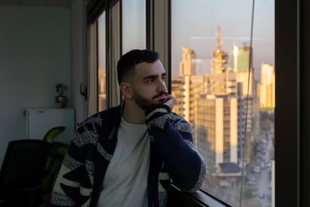 A young Arab man looks out of a window in a tower block at a city skyline