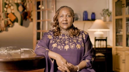A woman with long hair and a gold embroidered top sitting in a living room