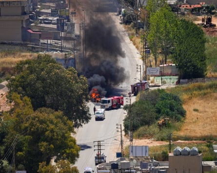 High-angle view of a burning vehicle in a road, with ambulance and fire trucks parked beside it