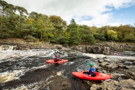 Two kayaks in rapids on rocky river with trees on bankside