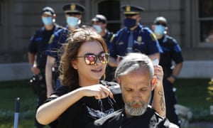 A hairstylist gives a free haircut as police watch outside the state capitol in Lansing, Michigan, on 20 May.