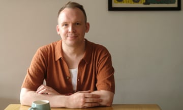 Samuel Burr sitting at a table, smiling and looking relaxed, with a mug of coffee on the table