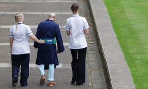 Two NHS staff walk with an older patient outside St Thomas' Hospital in London