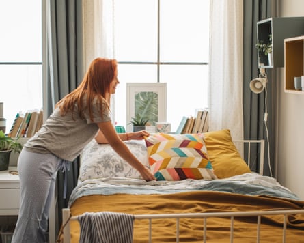 Young woman at dorm room. It is morning and she is making bed while listening music on headphones.