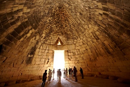 People standing in a large beehive-shaped stone tomb with light coming through an entrance