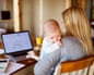 A mother using a laptop at home while holding her baby