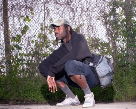 The musician Dev Hynes is crouching looking into a pond.