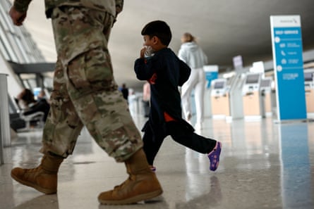 A small boy walks through an airport. A serviceman walks next to him, only his legs can be seen