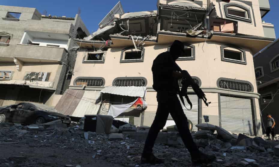 A Palestinian militant walks past the home of the Islamic Jihad commander Baha Abu al-Ata after it was bombed by Israel.