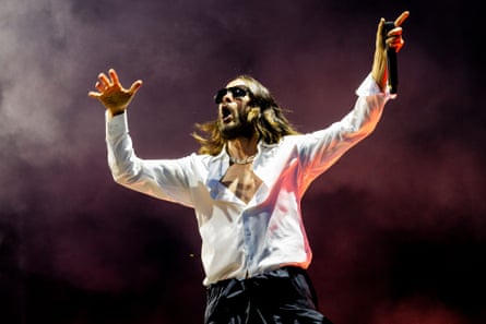 Leto on stage with Thirty Seconds To Mars in Milan last year: he is singing with his arms outstretched, a microphone in one hand. He wears a part-unbuttoned white shirt and black trousers.