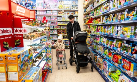 a father strolls through the aisles of games and toys  in a toy shop with a pram and his two-year-old daughter