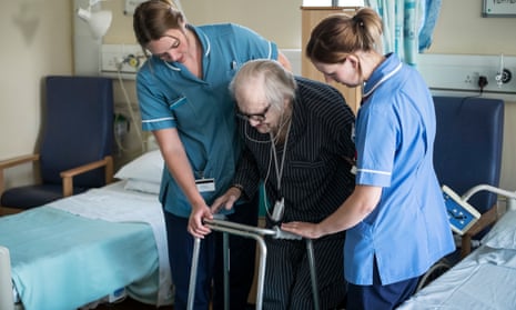 two nurses help an elderly woman with a walking frame