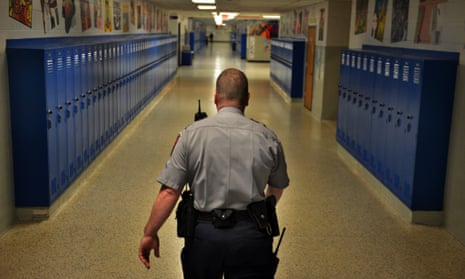A police officer patrols the hallways of a high school. 
