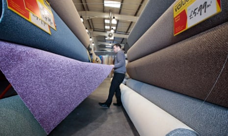 A sales representative arranges a display of carpet rolls at a Carpetright store