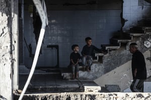 Children sit on some steps in a destroyed building