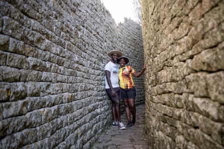 A young couple stand in a passageway between two high walls of carved stones 