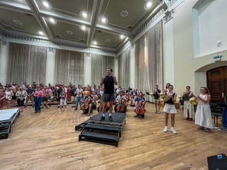 An orchestral rehearsal with a man standing on a small black platform with many people behind him