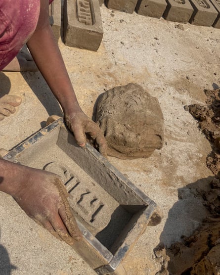 The hands of someone squatting down are seen with a large rectangular mould and a ball of clay