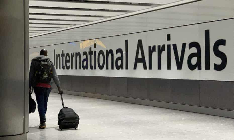 A man pulling a suitcase walks past international arrivals sign at Heathrow