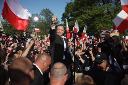 Karol Nawrocki gives a two finger V peace-sign gesture to a crowd of people waving Polish national flags