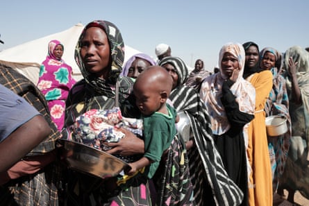 Women stand in line with empty bowls and holding babies to receive food aid