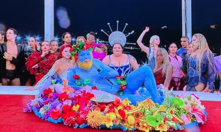 a man covered in blue body paint sat on a bed of brightly coloured flowers